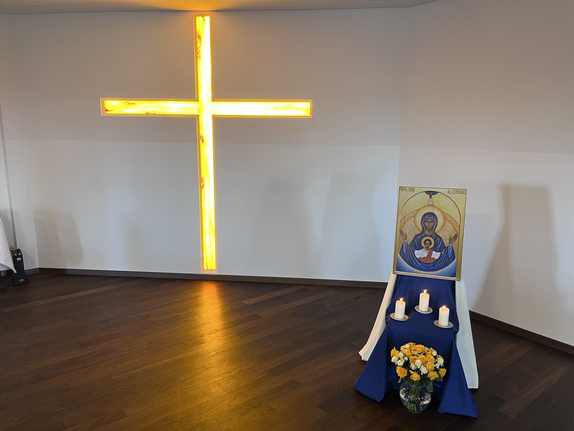 Ein leuchtendes Kreuz an der Wand eines stillen Raumes, davor eine Marienikone